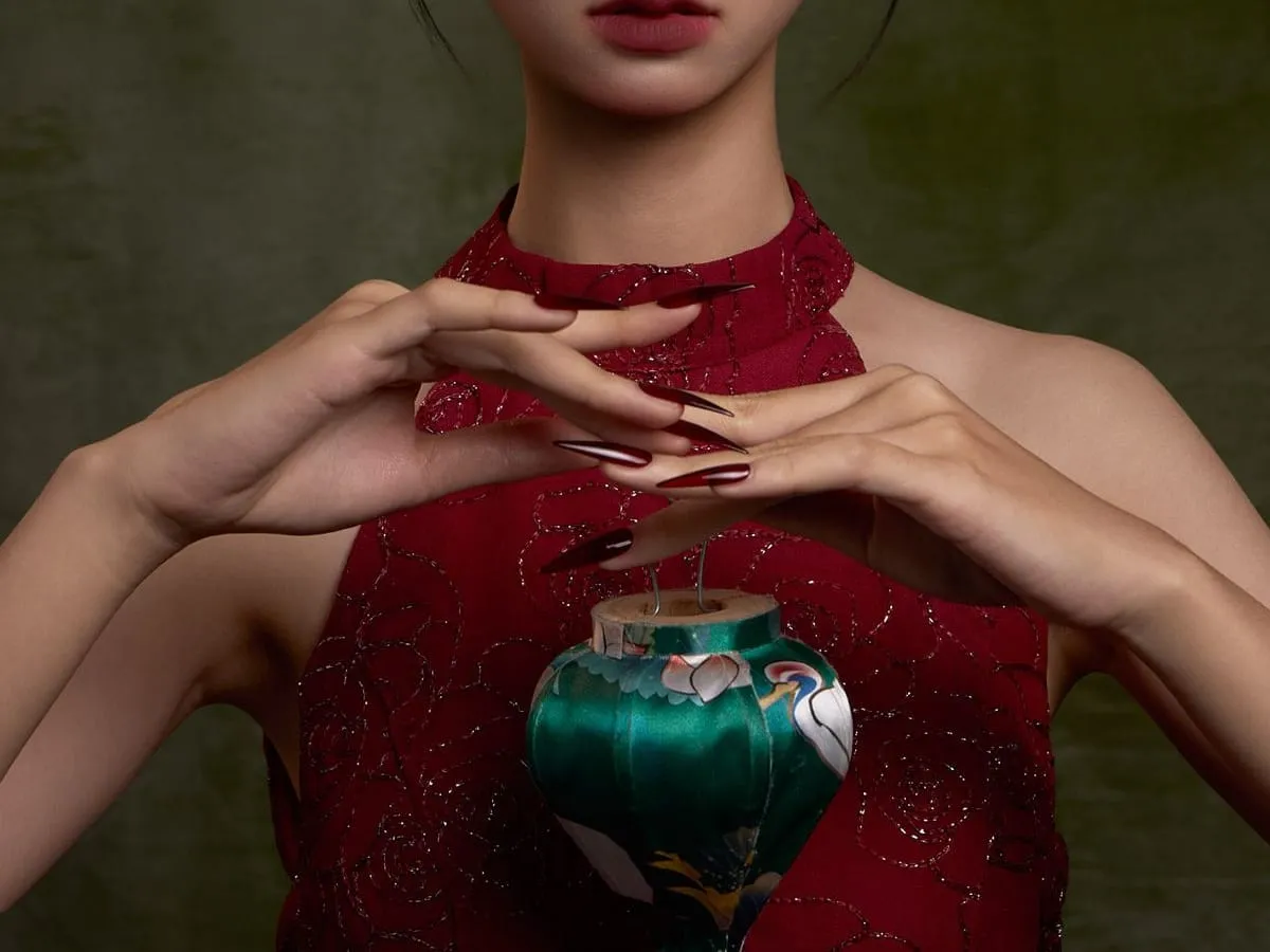 A hand holding a glass lantern, soft light on a moss-green backdrop