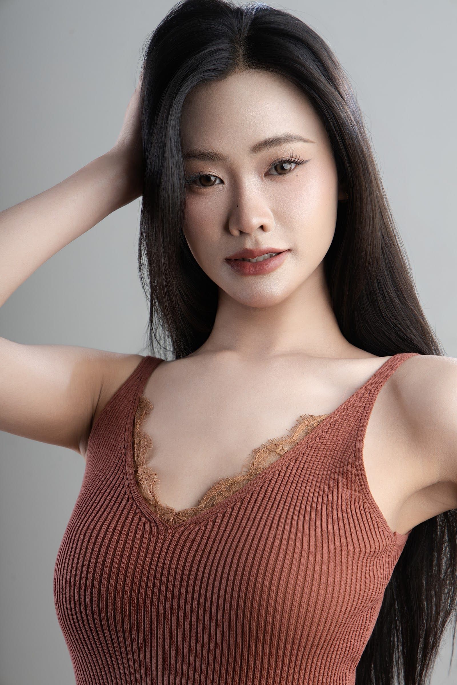 Full length of a woman in a terracotta camisole, hand resting on her dress, light grey backdrop