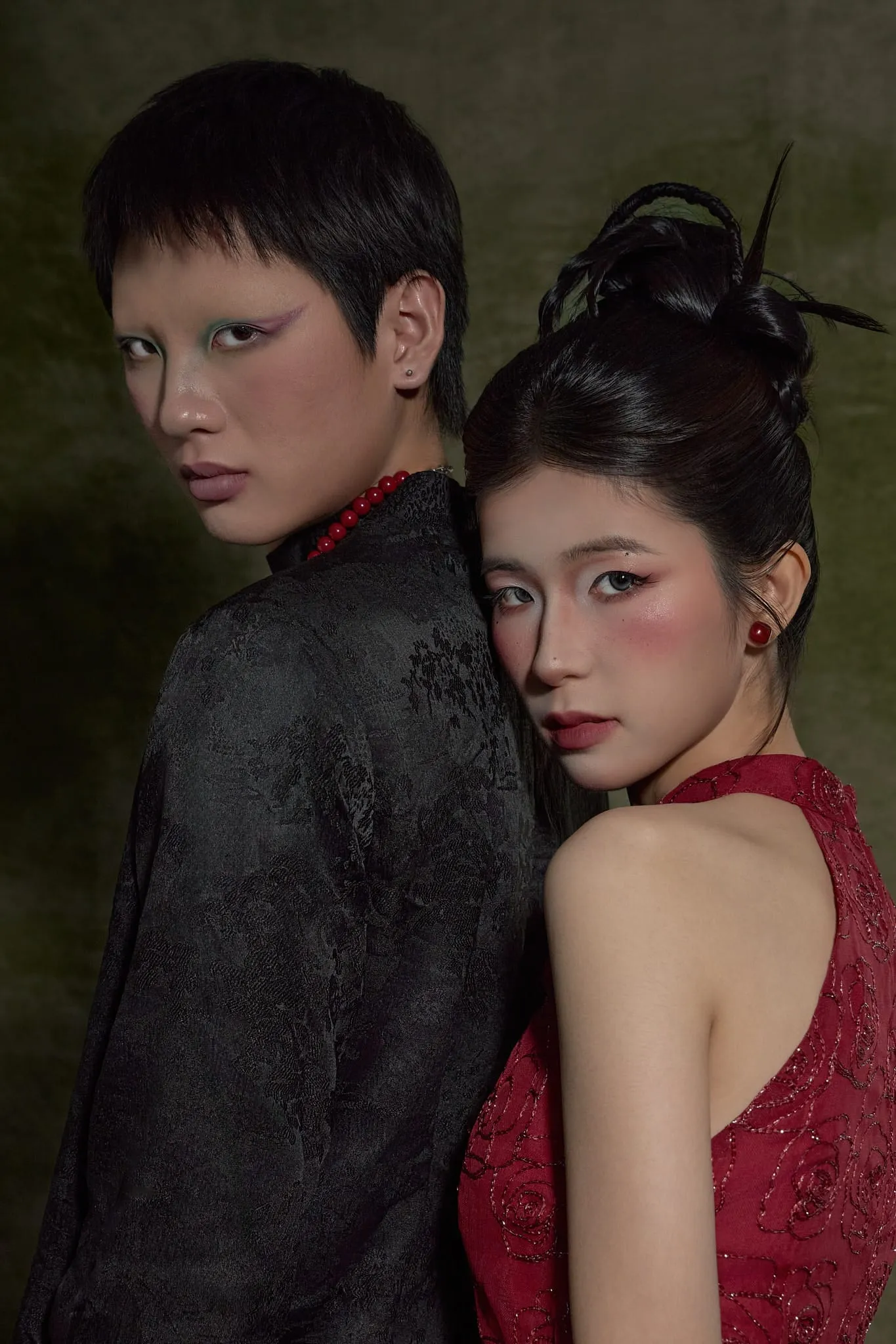 A couple in black and red standing close together on a moss-green backdrop