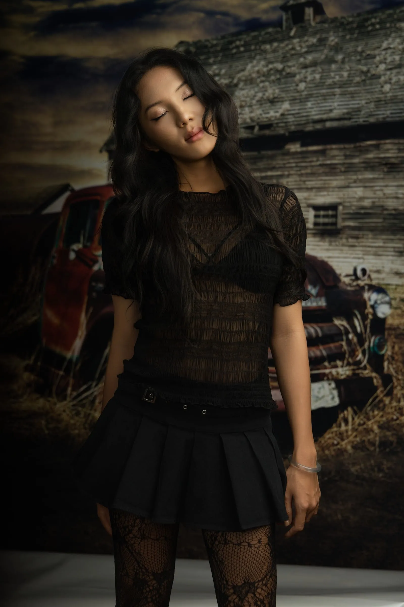 Country concept: a black lace top and pleated skirt with an old car and a wooden barn behind