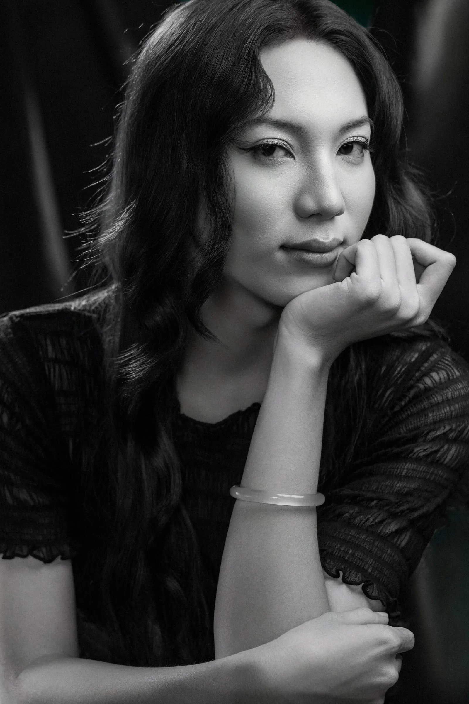 Black and white portrait: a woman resting her chin on her hand in a lace top, glancing aside