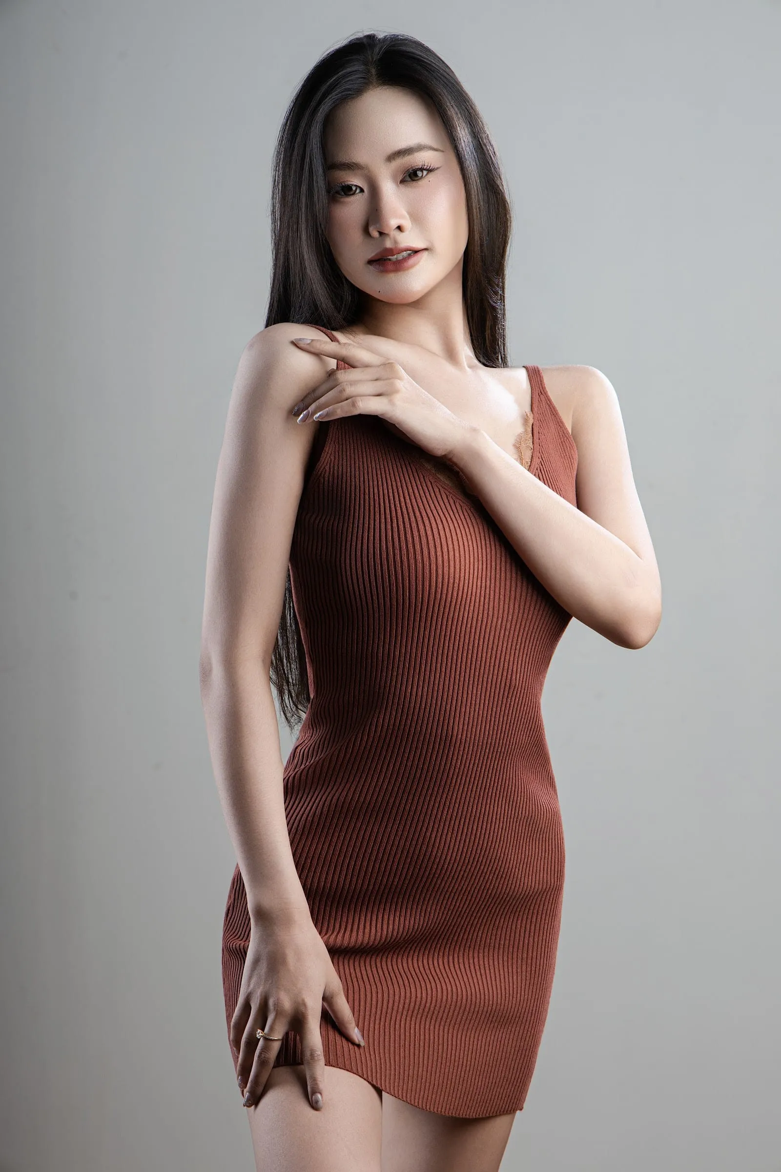 Full length of a woman in a terracotta camisole, hand resting on her dress, light grey backdrop