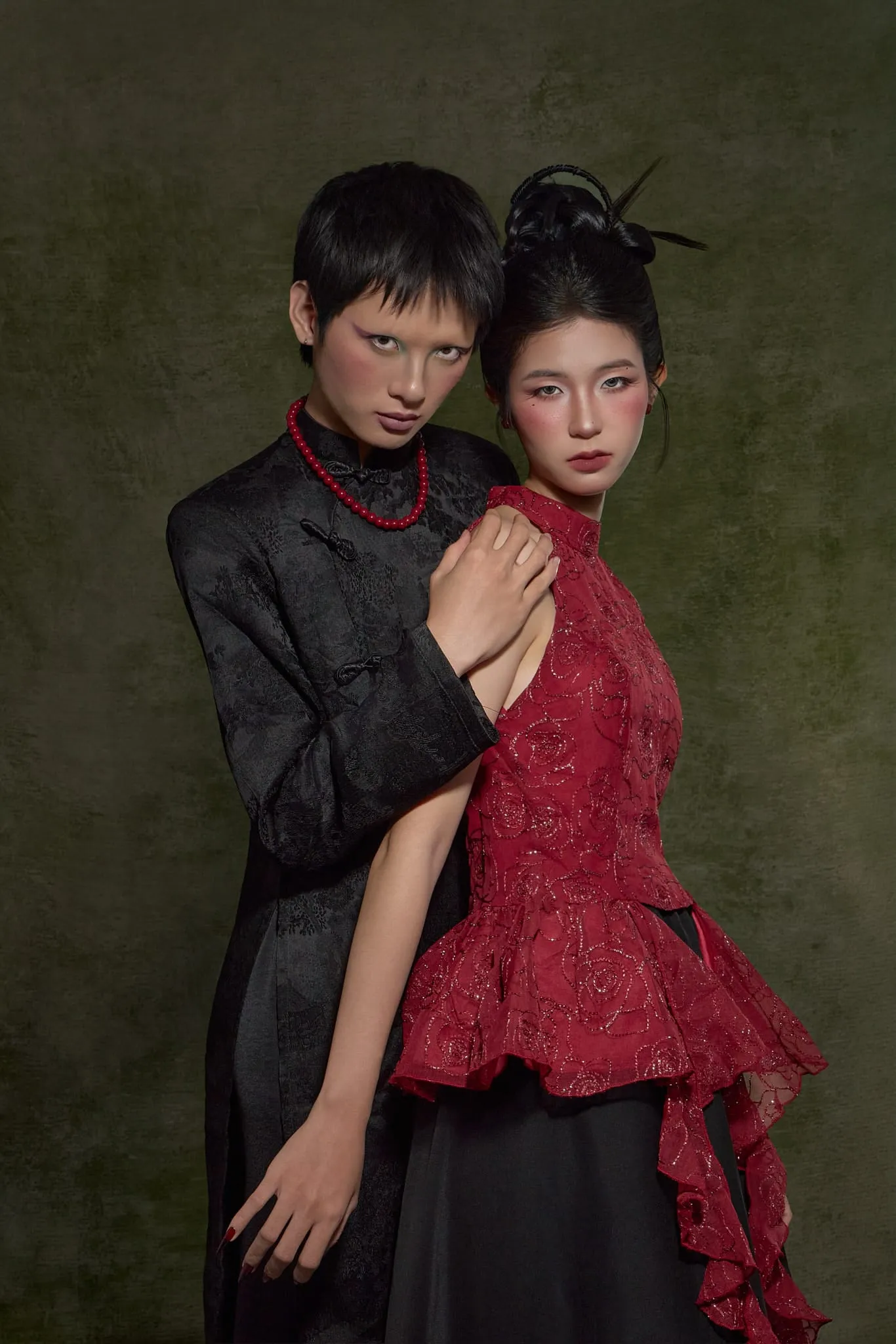 A couple in black and red standing close together on a moss-green backdrop