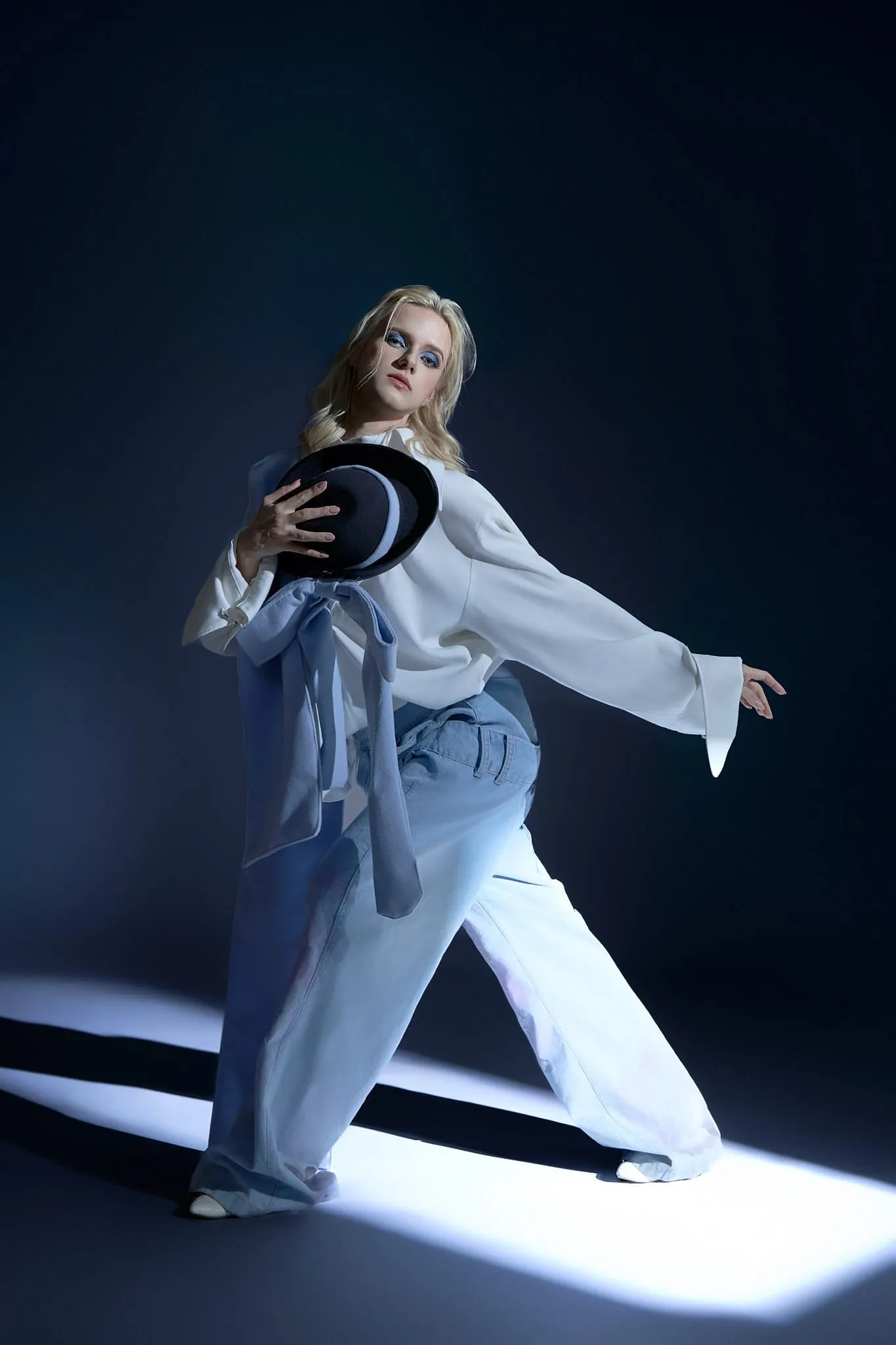 A model in a white jacket and wide jeans striding through a streak of blue light on a dark backdrop