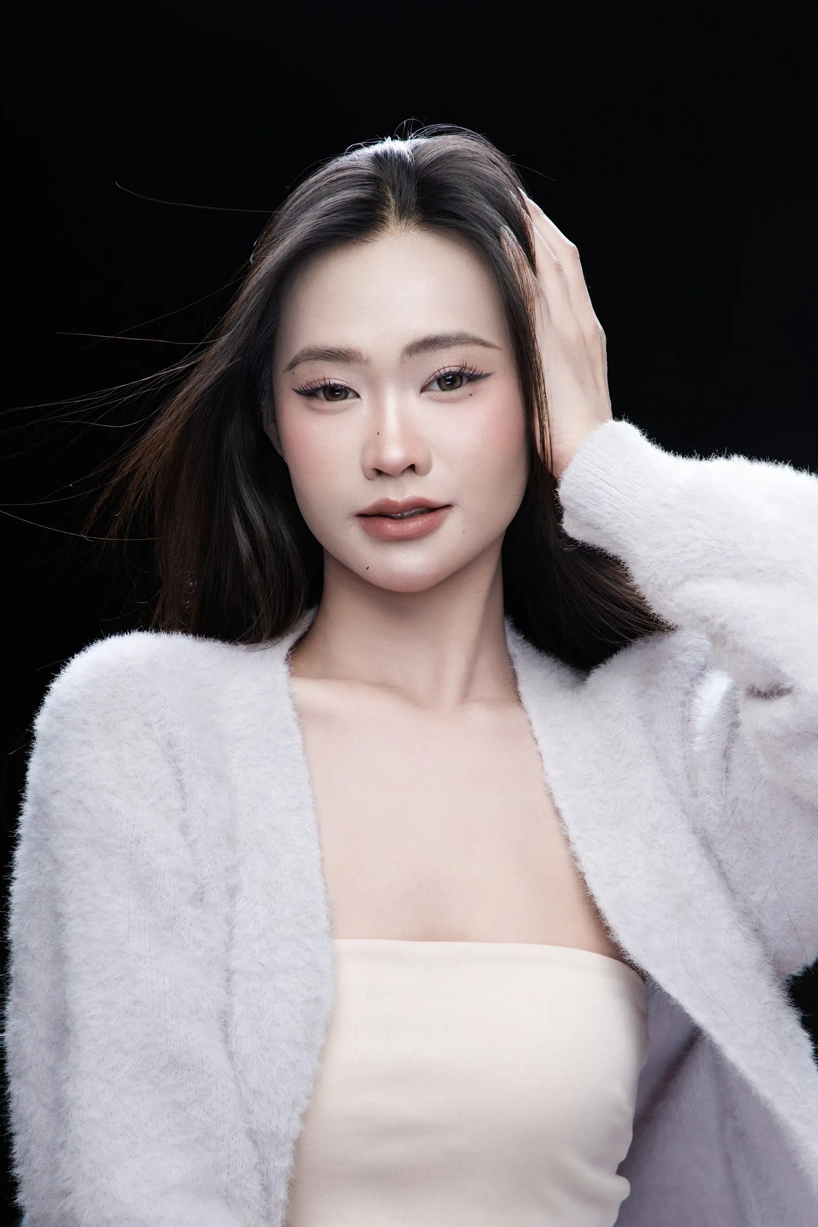 Portrait of a woman with long black hair in a white cardigan against a black backdrop