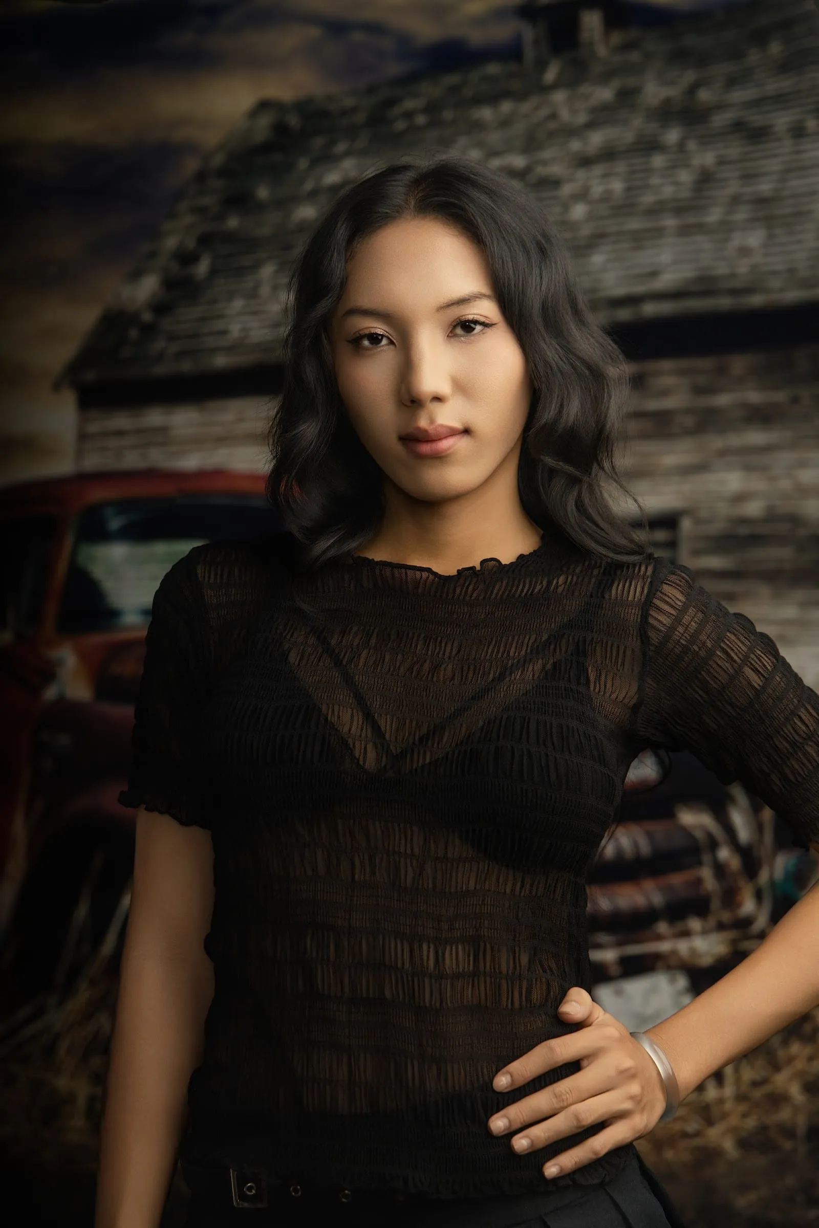 A woman with long hair in a black lace top in front of an old wooden barn